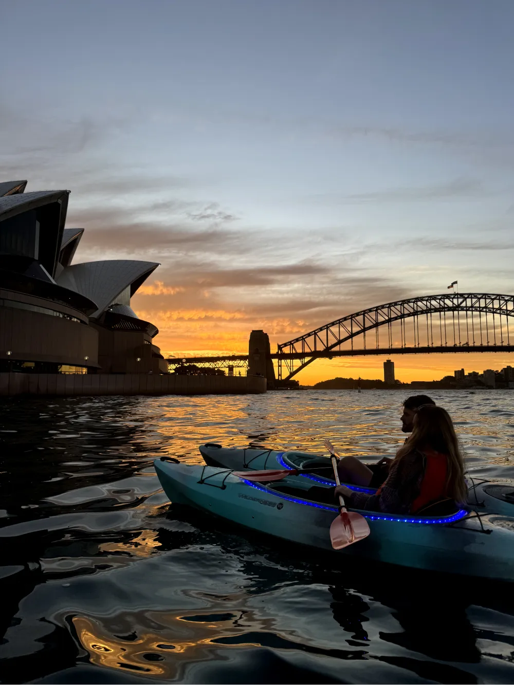 Couple kayaking near the Sydney Opera House and Harbour Bridge during sunrise